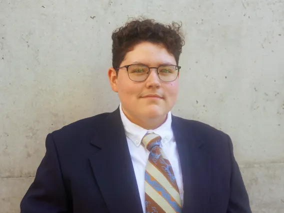 A photo of Francisco wearing a dapper navy suit with a white undershirt and a striped brown, cream, and light blue tie. 