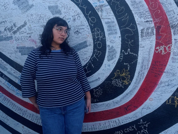 Photo of Ashley standing against a wall with lots of graffiti