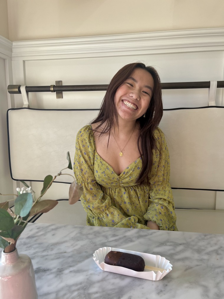 A photo of Allie sitting at a table with a dessert in front of her. She is smiling at the camera, and is wearing a green top. Her hair is down and over her shoulders.