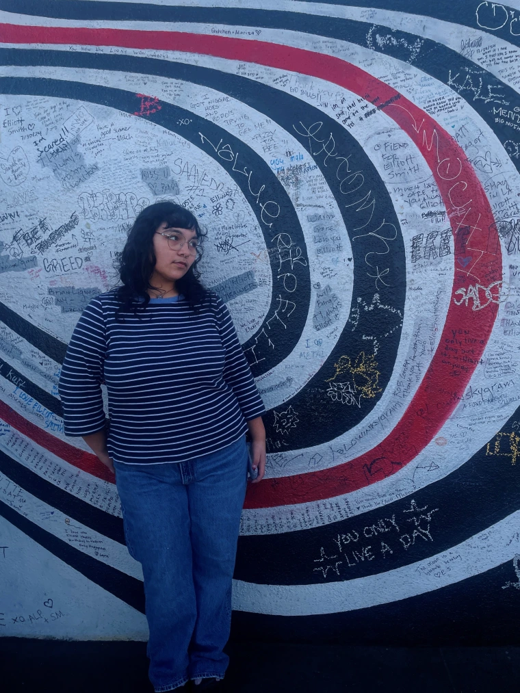 Photo of Ashley standing against a wall with lots of graffiti